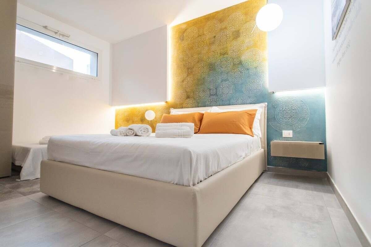 Une chambre à coucher moderne avec un grand lit, une tête de lit ornée d’un motif géométrique et une table de chevet avec une lampe.