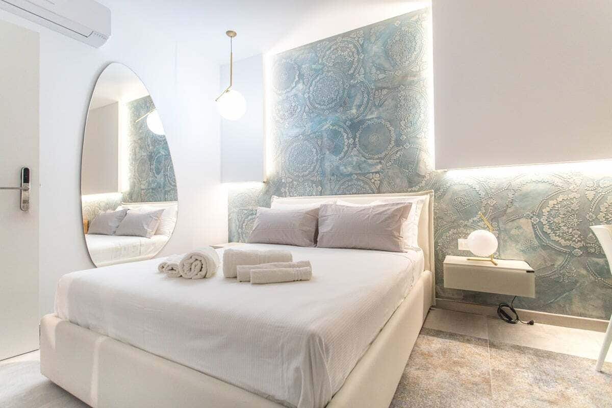 Une chambre moderne avec un grand lit, une table de chevet avec une lampe et un mur orné d’un motif décoratif.