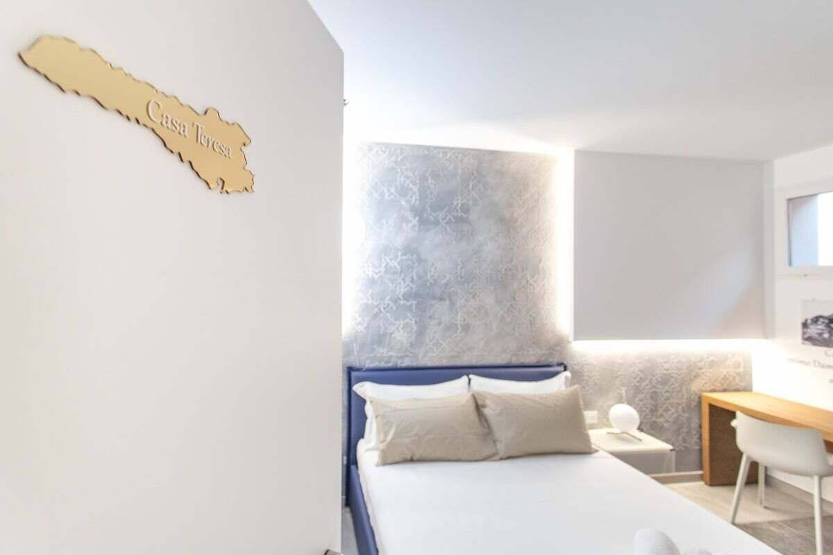 Une chambre avec un lit, un bureau et une chaise. Il y a une étagère fixée au mur, sur laquelle est posé un objet décoratif, ainsi qu’une lampe fixée au mur.