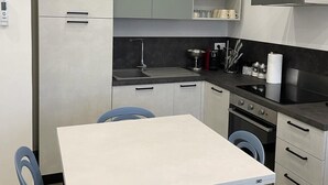Une cuisine compacte avec un coin repas, comprenant une table blanche, des chaises bleues et des appareils électroménagers modernes.