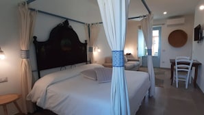 A bedroom with a four-poster bed, a bedside table, a chair, and a round wall decoration. - Lispusada B&B (Sassari)