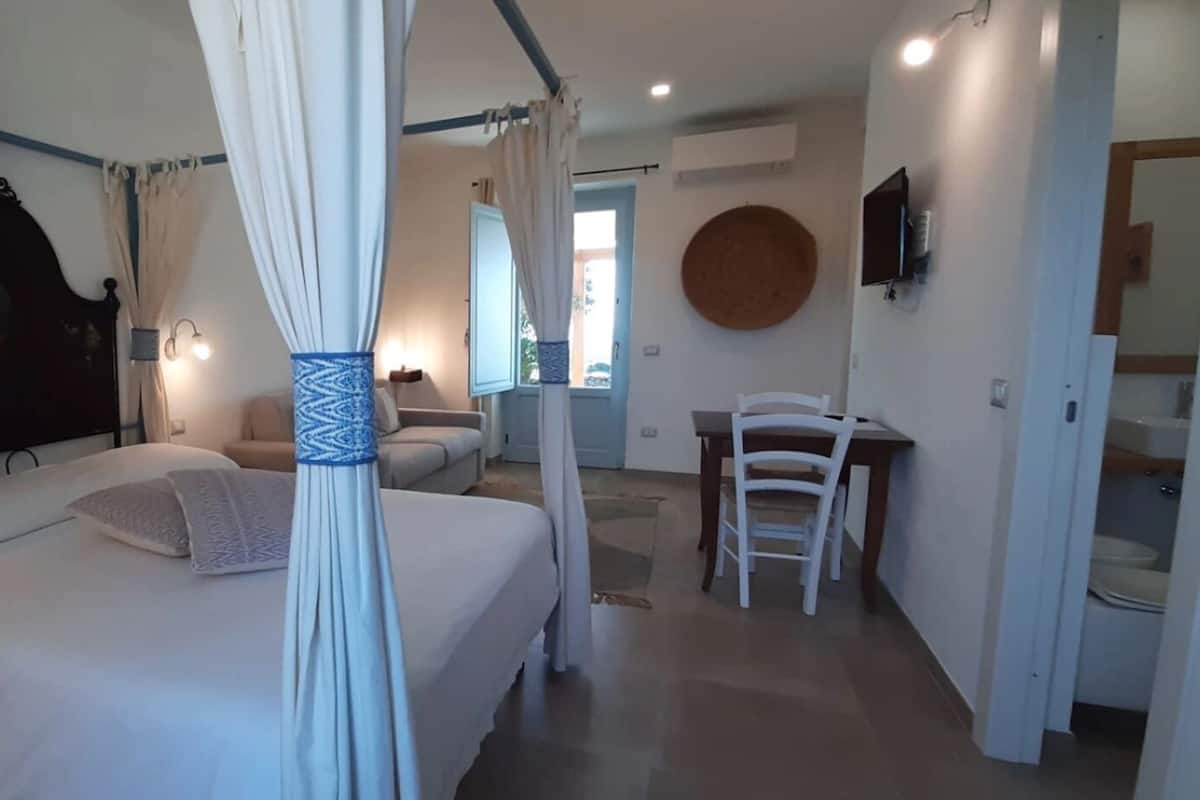 A bedroom with a four-poster bed, a bedside table, a chair, and a round wall decoration.