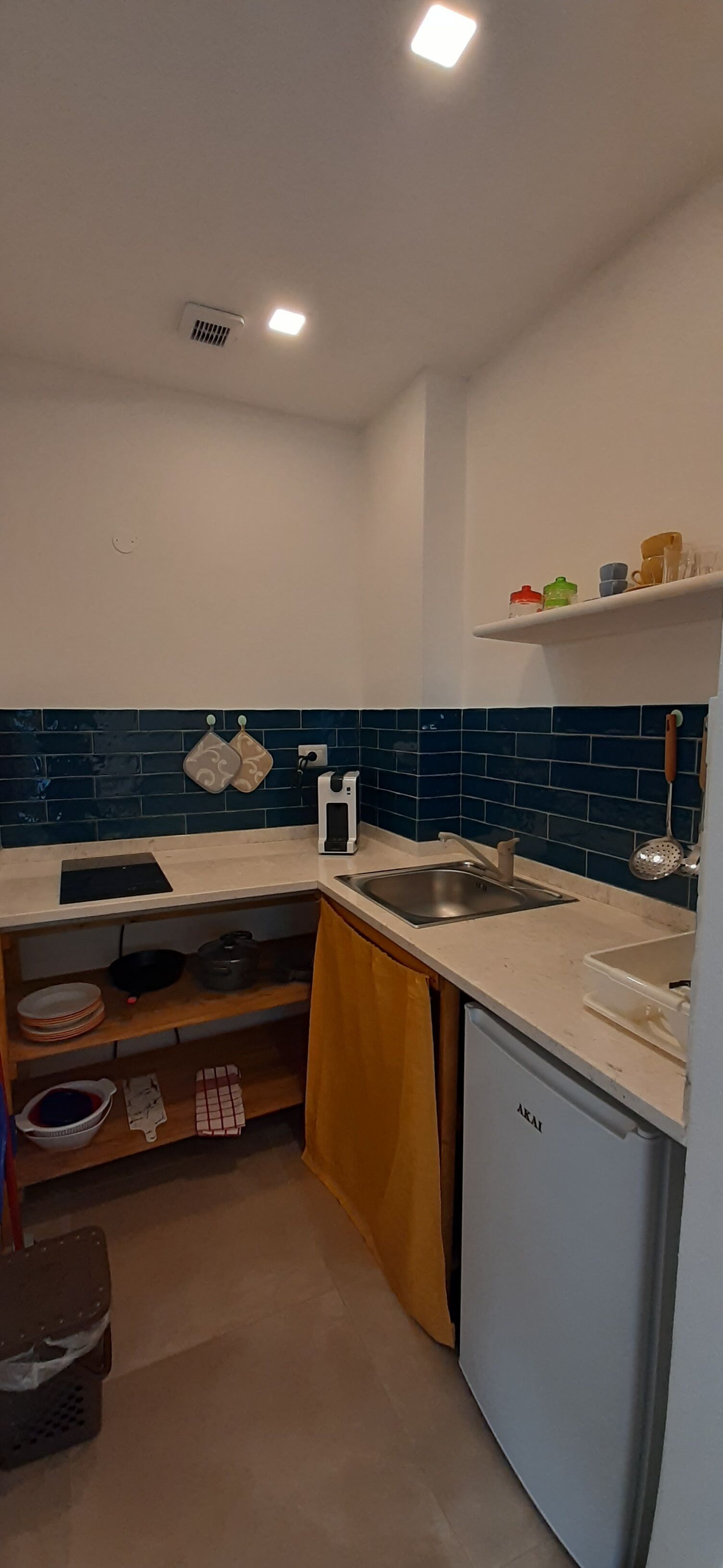 A compact kitchen with a sink, stove, and a dishwasher. There are shelves with dishes and a small countertop.