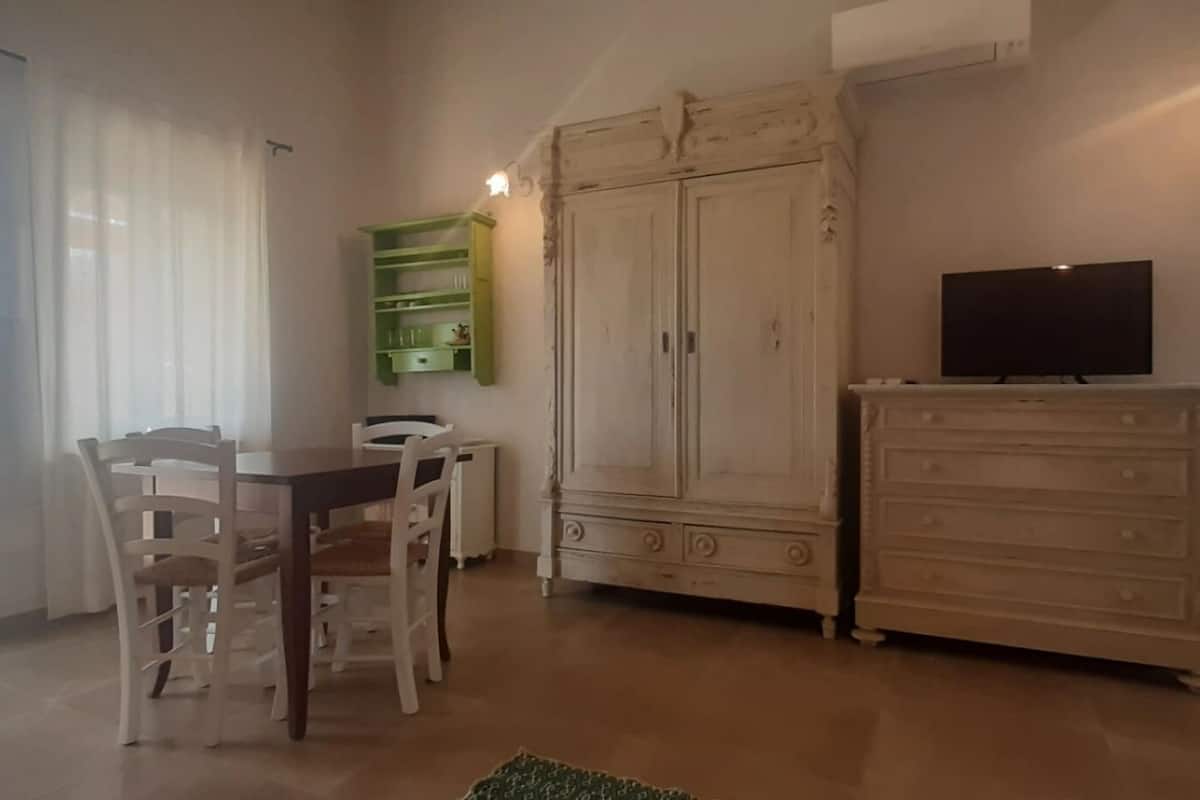 A dining area with a table and chairs, a cabinet with a television, and a large wardrobe.