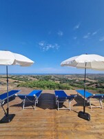Una terraza con sillas reclinables azules y sombrillas blancas, con vista a un paisaje pintoresco.