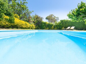 Una piscina azul cristalina con sillones de descanso a la derecha.