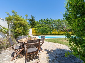 Une terrasse extérieure avec une table et des chaises, une piscine et un jardin agrémenté de diverses plantes et fleurs.