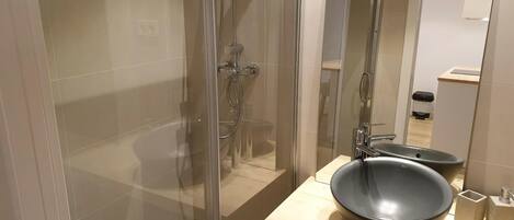 A modern bathroom with a glass-enclosed shower, a wooden vanity with a large black basin, and a mirror reflecting the room.