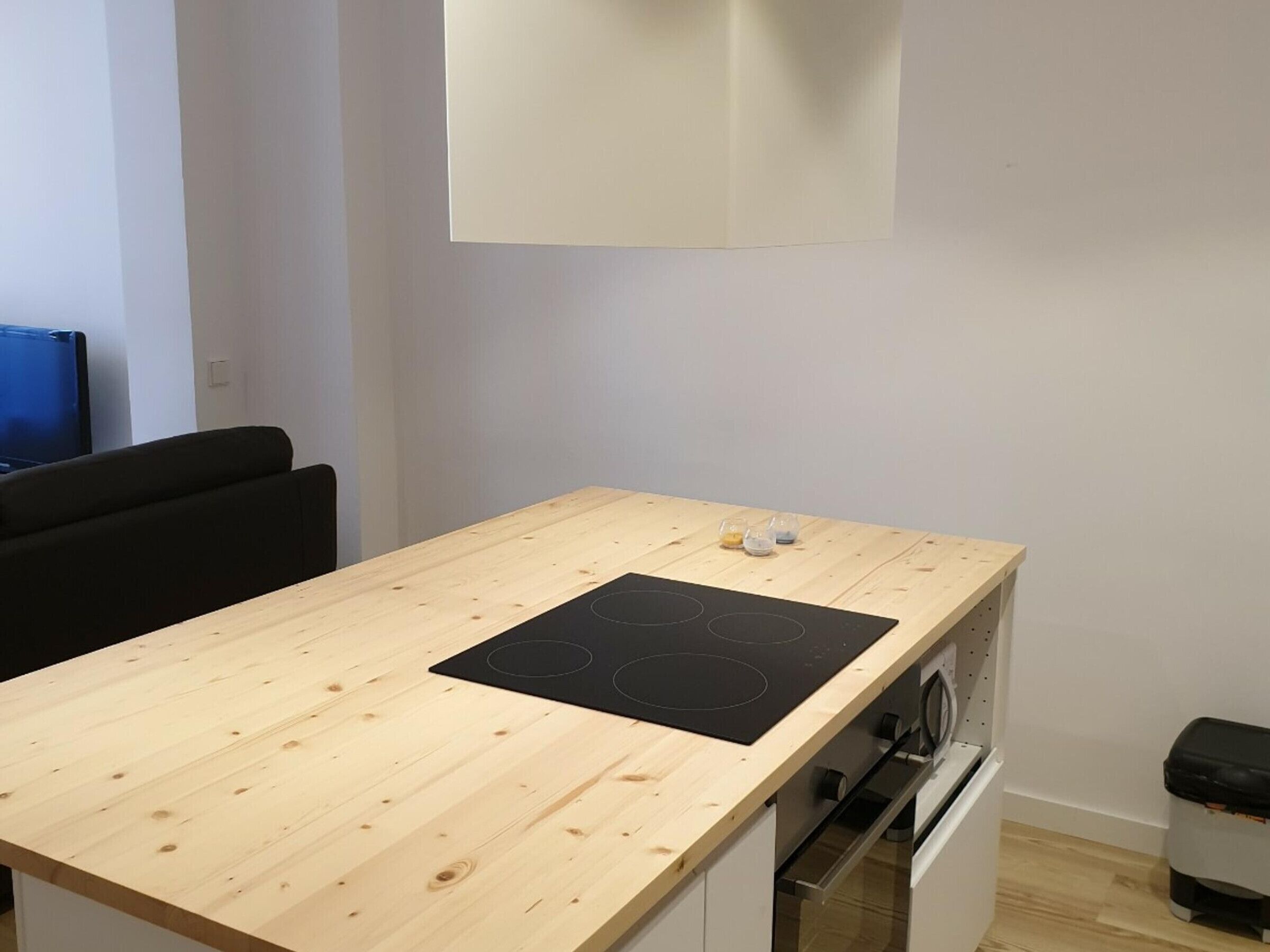 A small kitchen with a wooden countertop, a black induction cooktop, a built-in oven, and a white wall.