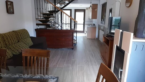 Ein geräumiger Wohnbereich mit einer Holztreppe, einem Esstisch mit Stühlen und einer Küchenzeile im Hintergrund.