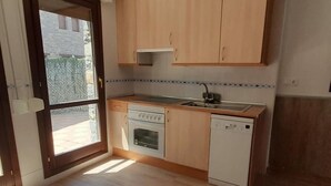 Eine kompakte Küche mit Holzausstattung, einem eingebauten Ofen, einer Spülmaschine und einem Fenster für natürliches Licht.