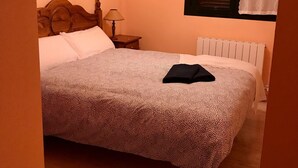 A neatly made bed with a patterned bedspread, a wooden headboard, a bedside lamp, and a radiator. - Family-Friendly Apartment with Pool, Balcony, and Parking in Jaca (Jaca)
