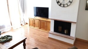A living room with a wooden cabinet, a flat-screen TV, a fireplace, and a wall clock. - Spacious 2-bedroom apartment with parking in Villanúa (Villanúa)