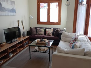 A living room with a TV, two sofas, a coffee table, and a window with curtains.