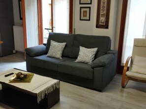 A living room with a grey sofa, two pillows, a small table with a magazine and a remote control, and a wooden chair. - Central Apartment for 4 with Parking in Jaca's Main Street (Jaca)