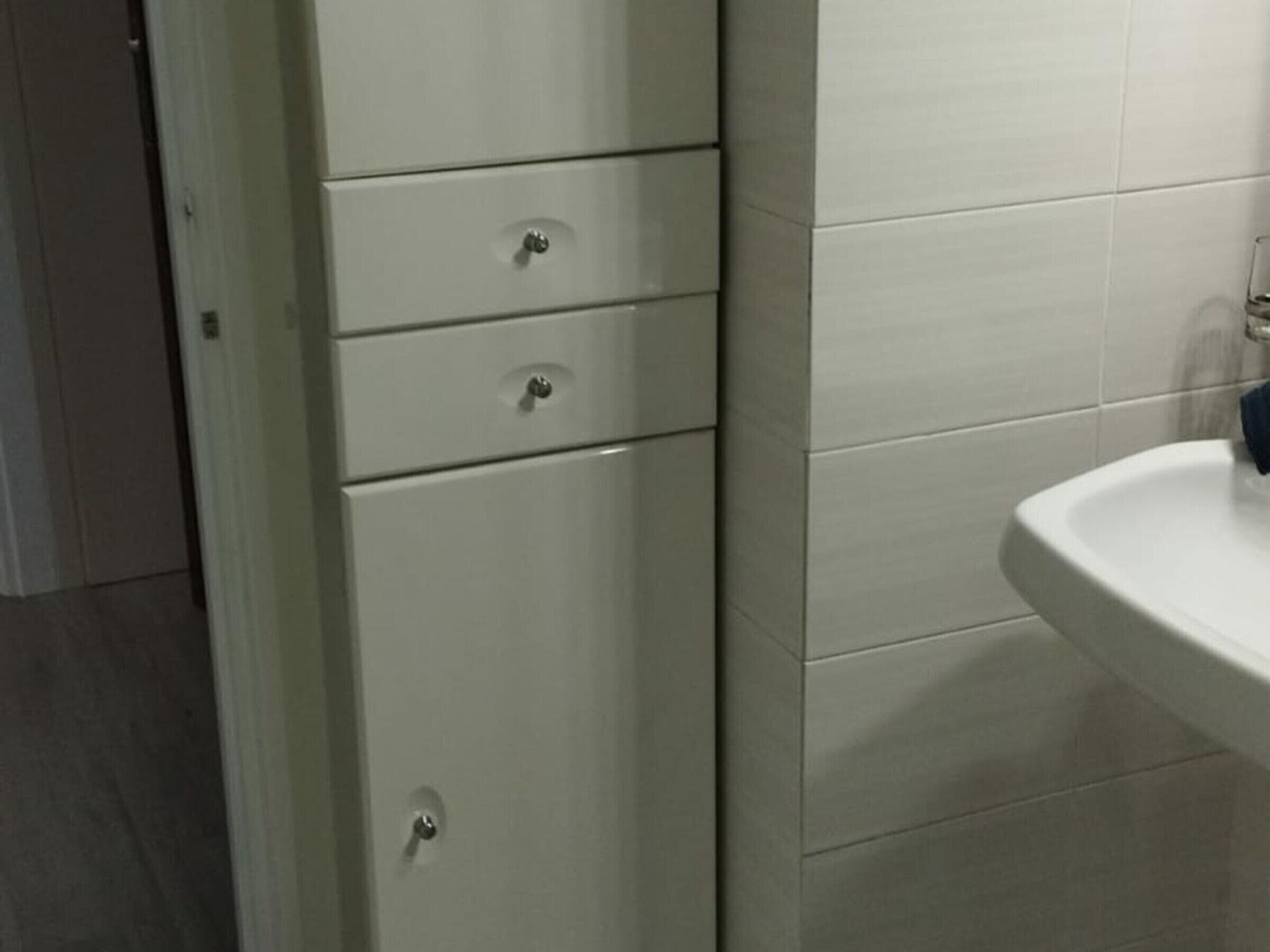 A bathroom with a white sink, a mirror, and a cabinet with three drawers.