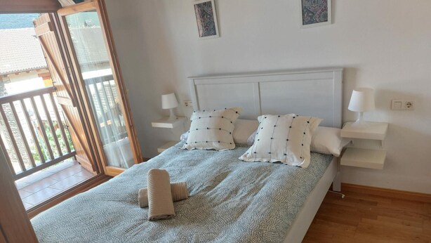 Een slaapkamer met een bed, twee nachtkastjes, een raam met uitzicht en een deur naar een buitenbalkon.