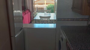 Een keuken met een zichtbare eethoek door een glazen deur, een wasmachine en een betegelde spatwand.