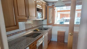Een keuken met houten kastjes, een granieten aanrechtblad, een ingebouwde oven, een vaatwasser en een raam met uitzicht op de straat.