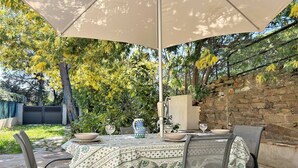 Een terras buiten met een tafel voor twee personen, omringd door stoelen, onder een grote parasol.