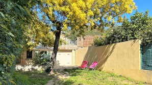 Een stenen pad leidt naar een huis met een garage, een hek en twee roze stoelen.