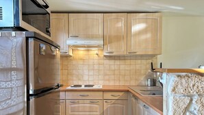 Een kleine keuken met houten kastjes, een roestvrijstalen koelkast, een inbouwoven en een magnetron.