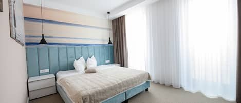A bedroom with a bed, a nightstand, a painting, a window with curtains, and a ceiling light.