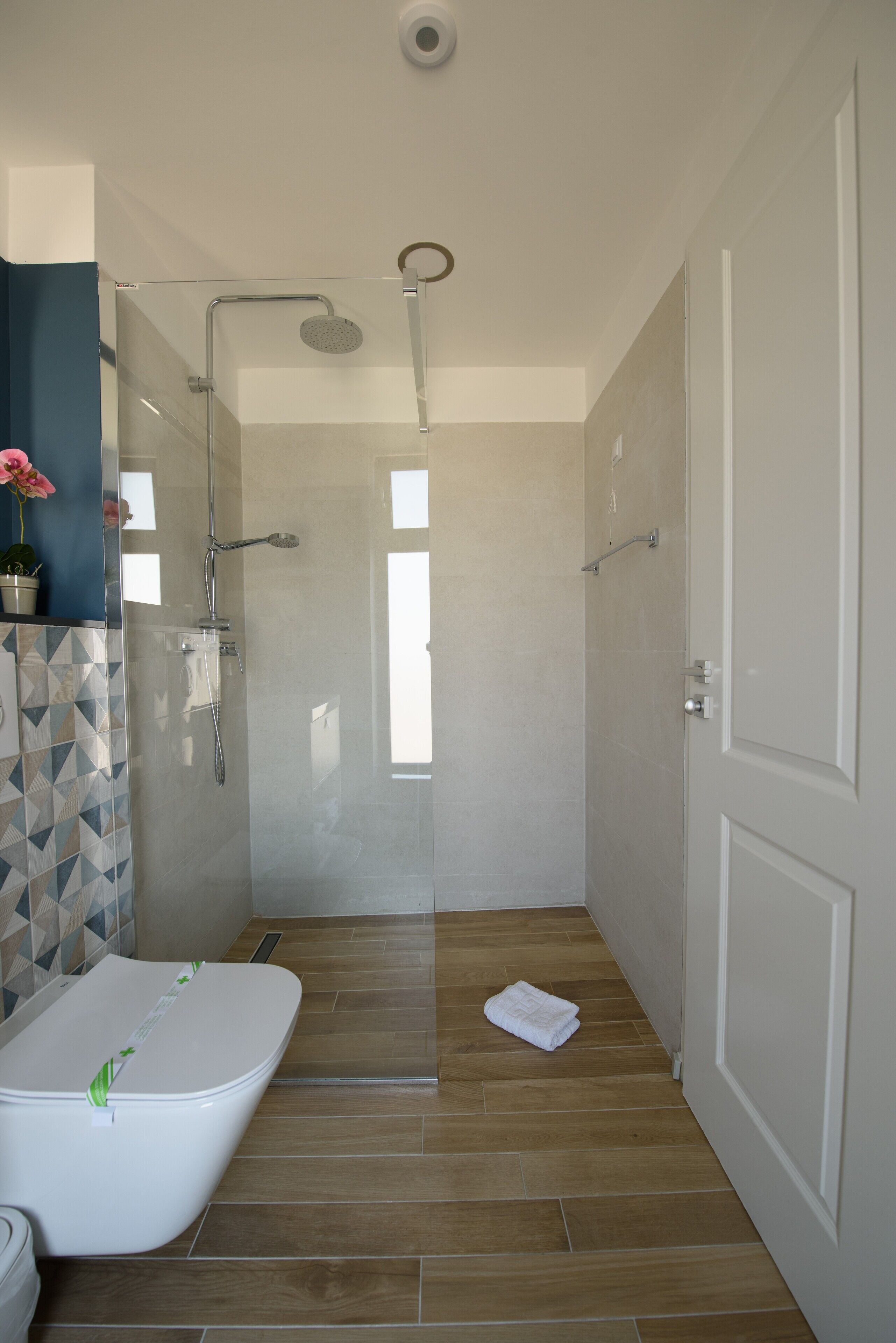 A modern bathroom with a glass-enclosed shower, a white bathtub, and a wooden floor.