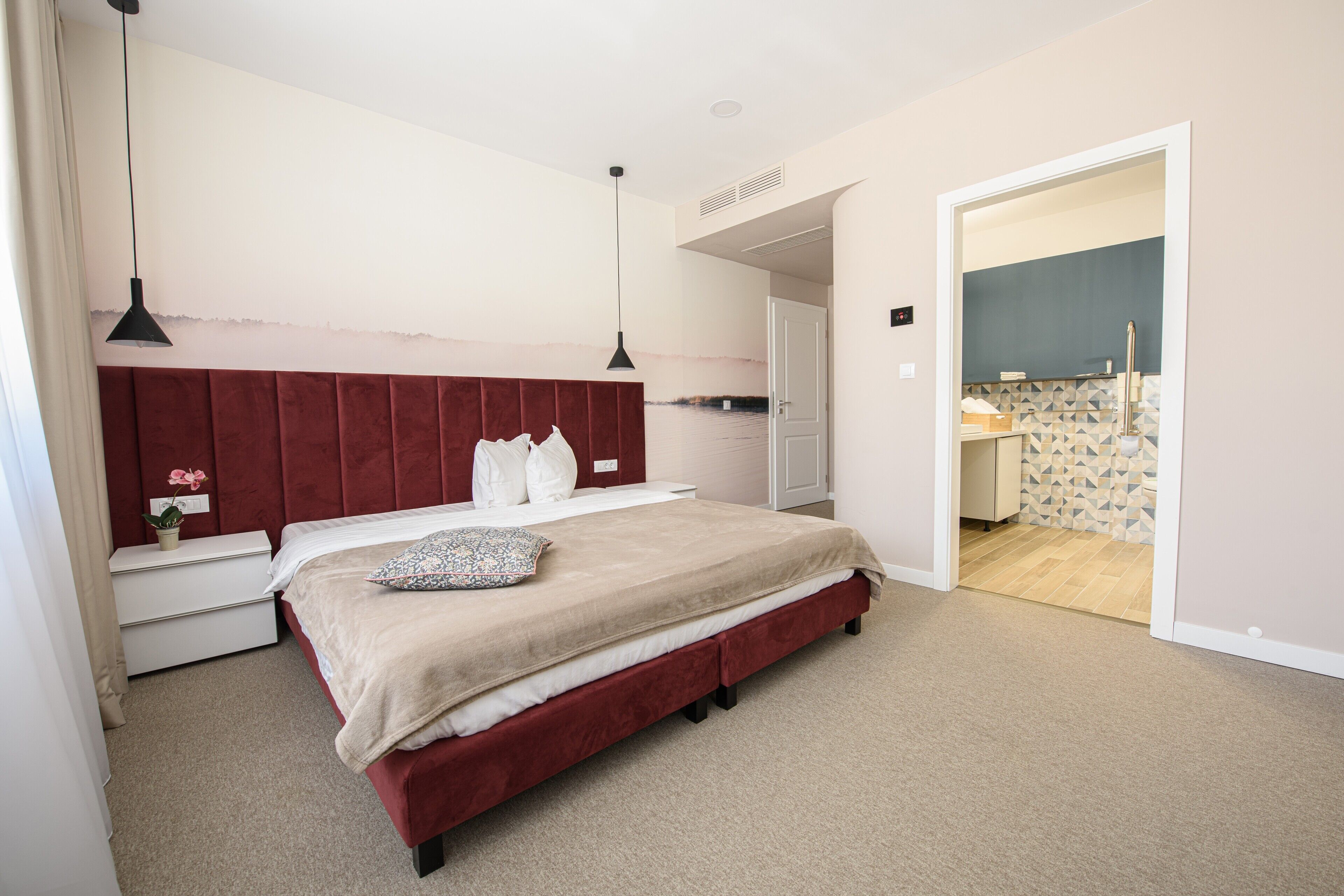 A bedroom with a large bed, a nightstand, a dresser, and a door leading to a bathroom.