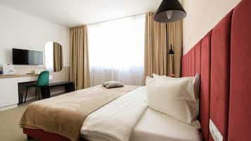 Una habitación de hotel con una cama, un escritorio con una silla, un televisor y una ventana con cortinas.