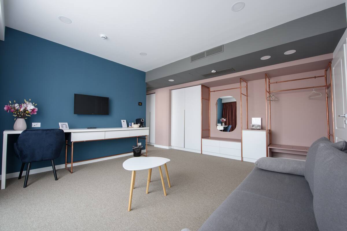 A modern room with a blue accent wall, a white desk, a grey sofa, and a walk-in closet with copper shelving.