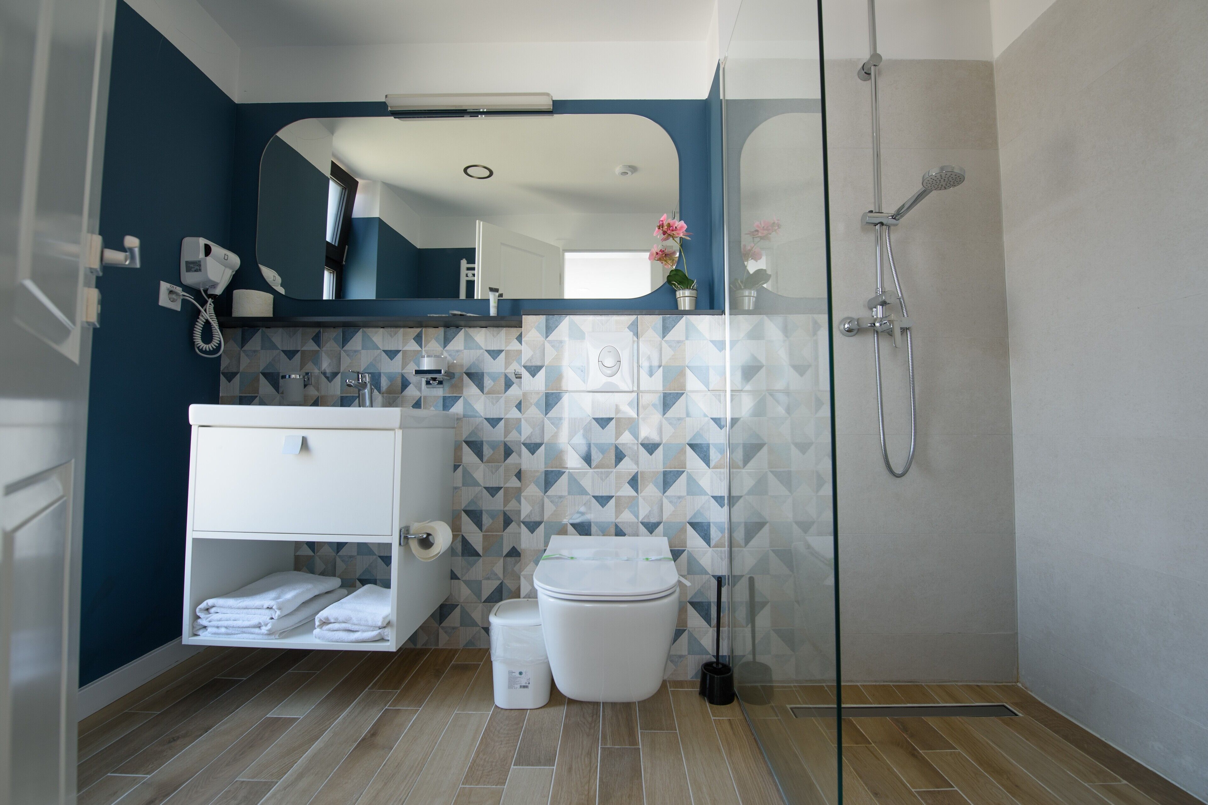 A modern bathroom with a blue accent wall, a white vanity, a glass shower enclosure, and a geometric tile backsplash.