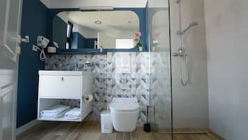A modern bathroom with a blue accent wall, a white vanity, a glass shower enclosure, and a geometric tile backsplash.