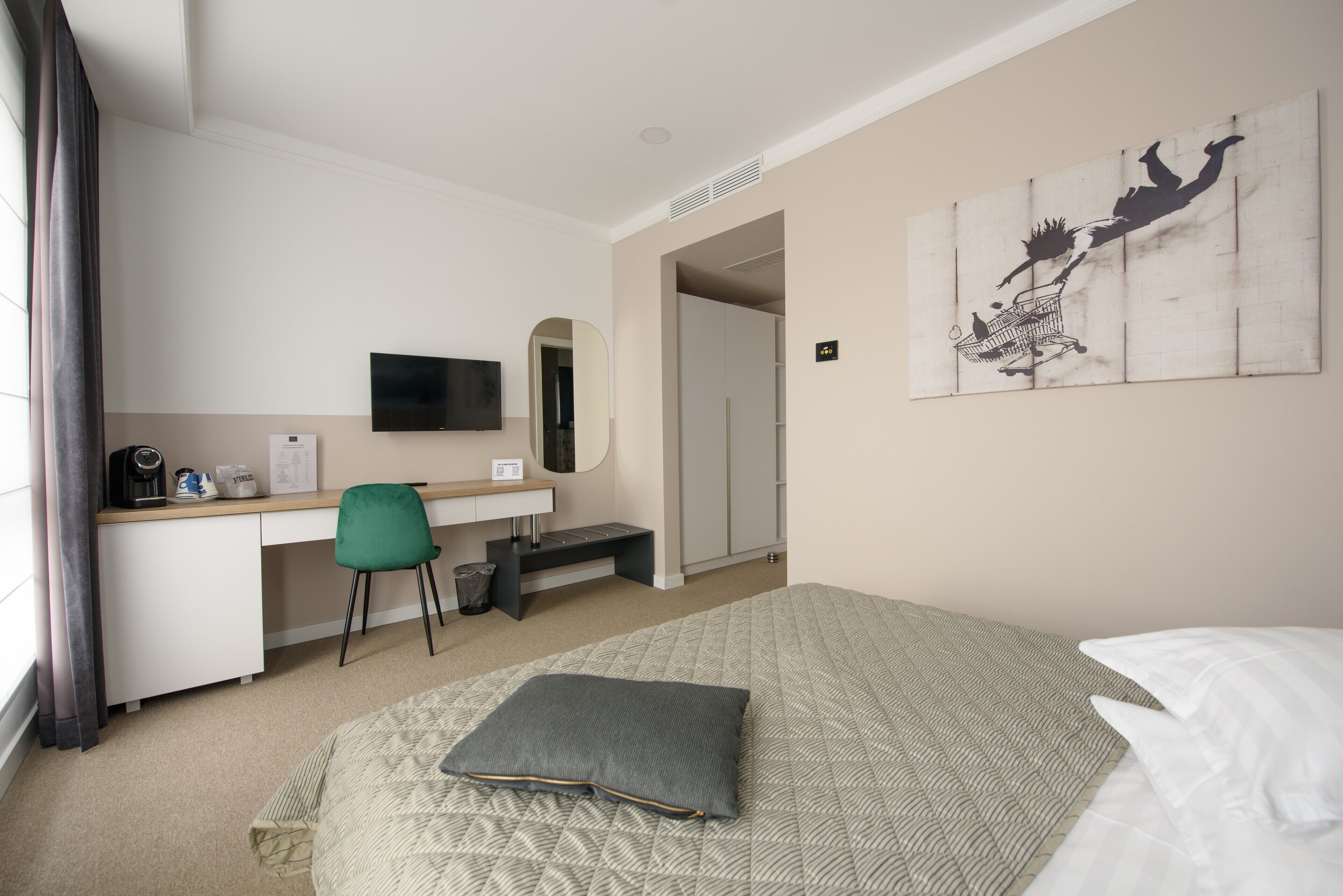 Habitación de hotel con cama, escritorio, silla, televisor, armario y un cuadro en la pared.