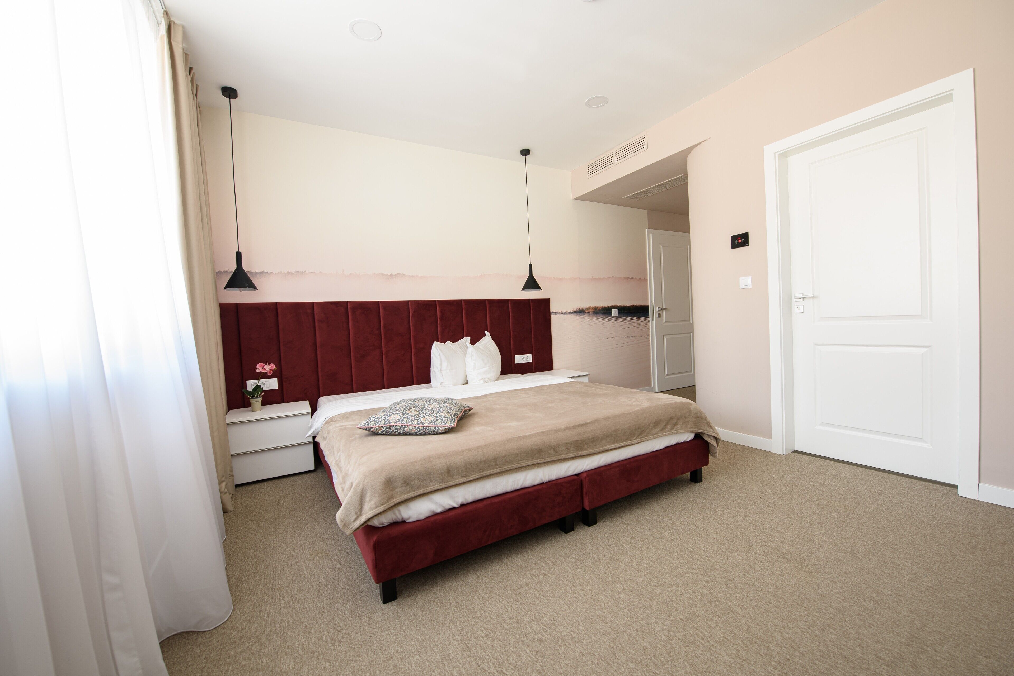 Quarto com uma cama grande, mesa de cabeceira, cômoda e porta.