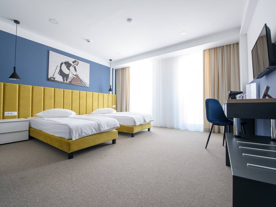 Habitación de hotel con dos camas, un escritorio, una silla, un televisor y un cuadro en la pared.