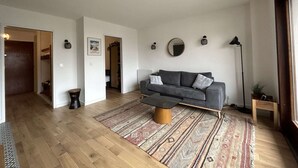 En rummelig stue med en grå sofa, et mønstret tæppe og et træbord.