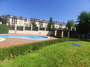 A swimming pool surrounded by a brick deck, with a hedge in the foreground and a row of apartment buildings in the background. - Lovely Apartment in Jaca with Pool Access (Jaca)