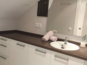 A modern bathroom with a white sink, a large mirror, and a dark countertop. There are two towels on the countertop and a power outlet on the wall. - Lovely Apartment in Jaca with Pool Access (Jaca)