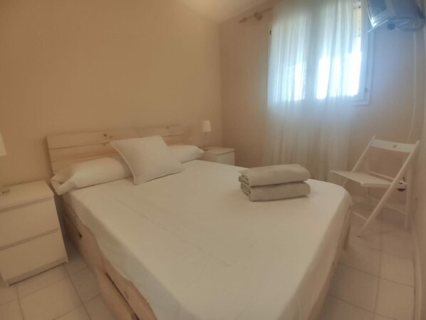 A neatly made bed with white linens, a bedside table with a lamp, and a chair to the right. - Lovely Apartment in Jaca with Pool Access (Jaca)