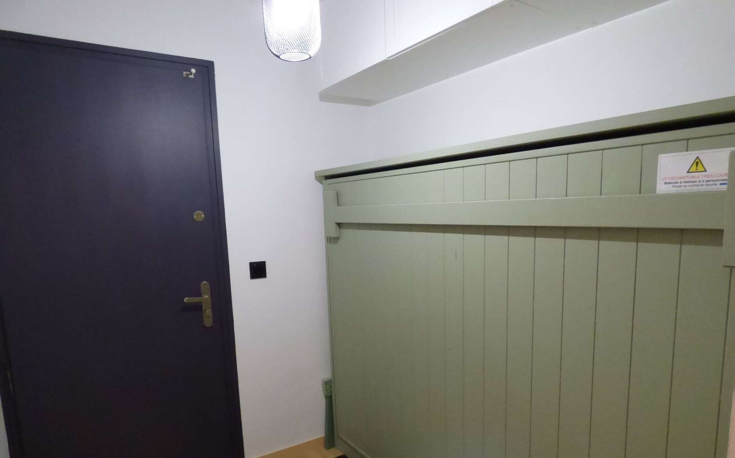 Une pièce avec une porte sombre, un radiateur vert clair et un panneau d’avertissement sur le mur.