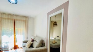 Un salon avec un canapé, un coin repas avec une chaise, et une vue sur une chambre à coucher avec un lit et un luminaire suspendu.