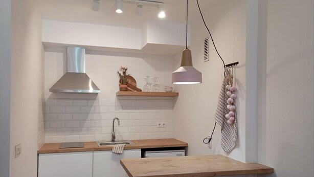 Une cuisine compacte avec des meubles blancs, un plan de travail en bois, une hotte de cuisine en acier inoxydable et des luminaires suspendus.