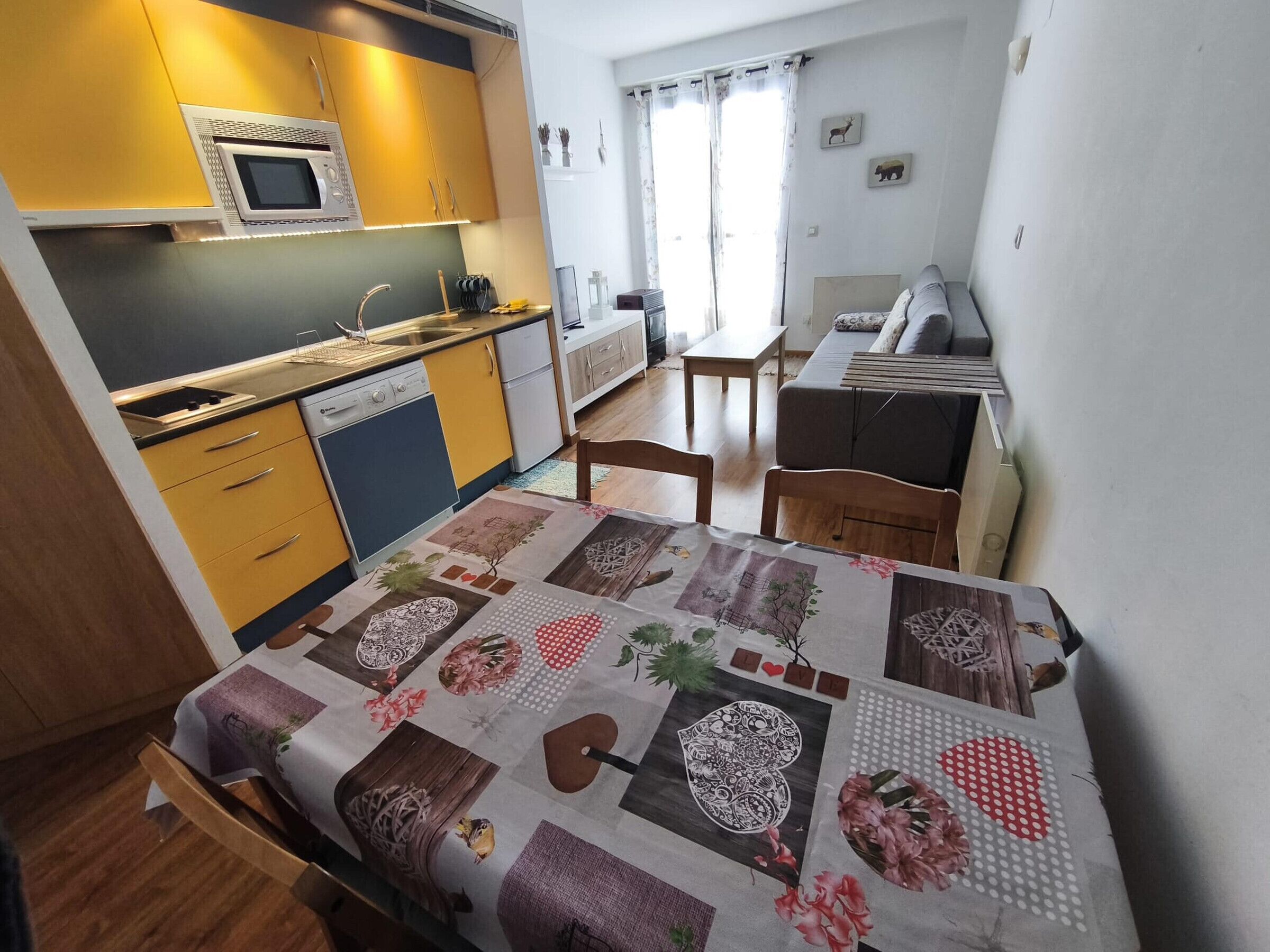 A compact kitchen with a microwave, stove, and dishwasher. There is a dining area with a table and chairs, and a bed with a floral bedspread.