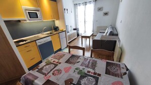 Eine kompakte Küche mit Mikrowelle, Herd und Geschirrspüler. Es gibt einen Essbereich mit Tisch und Stühlen sowie ein Bett mit blumigem Überwurf.