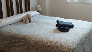 Ein ordentlich bezogenes Bett mit einer gemusterten Tagesdecke, einem gefalteten Handtuch und einem Teddybären auf den Kissen.