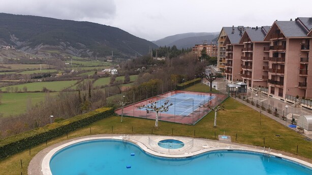 Une piscine avec un court de tennis, entourée d’un quartier résidentiel et avec des montagnes en arrière-plan.