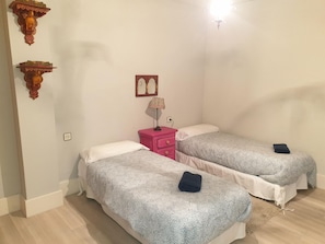 A small, well-lit room with two single beds, a pink nightstand with a lamp, and a wall-mounted mirror. - Cozy Mountain Apartment with Pool, Gym, and Parking near Jaca Center (Jaca)
