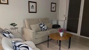 Un salon avec un canapé beige, un fauteuil à motifs, une petite table sur laquelle est posé un vase de fleurs et une porte-fenêtre coulissante.