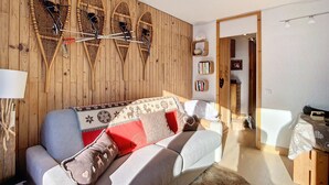 A cozy living room with a sofa, wooden wall paneling, a bookshelf, and a door leading to another room. - Cozy apartment at pistes, near shops (Méribel)